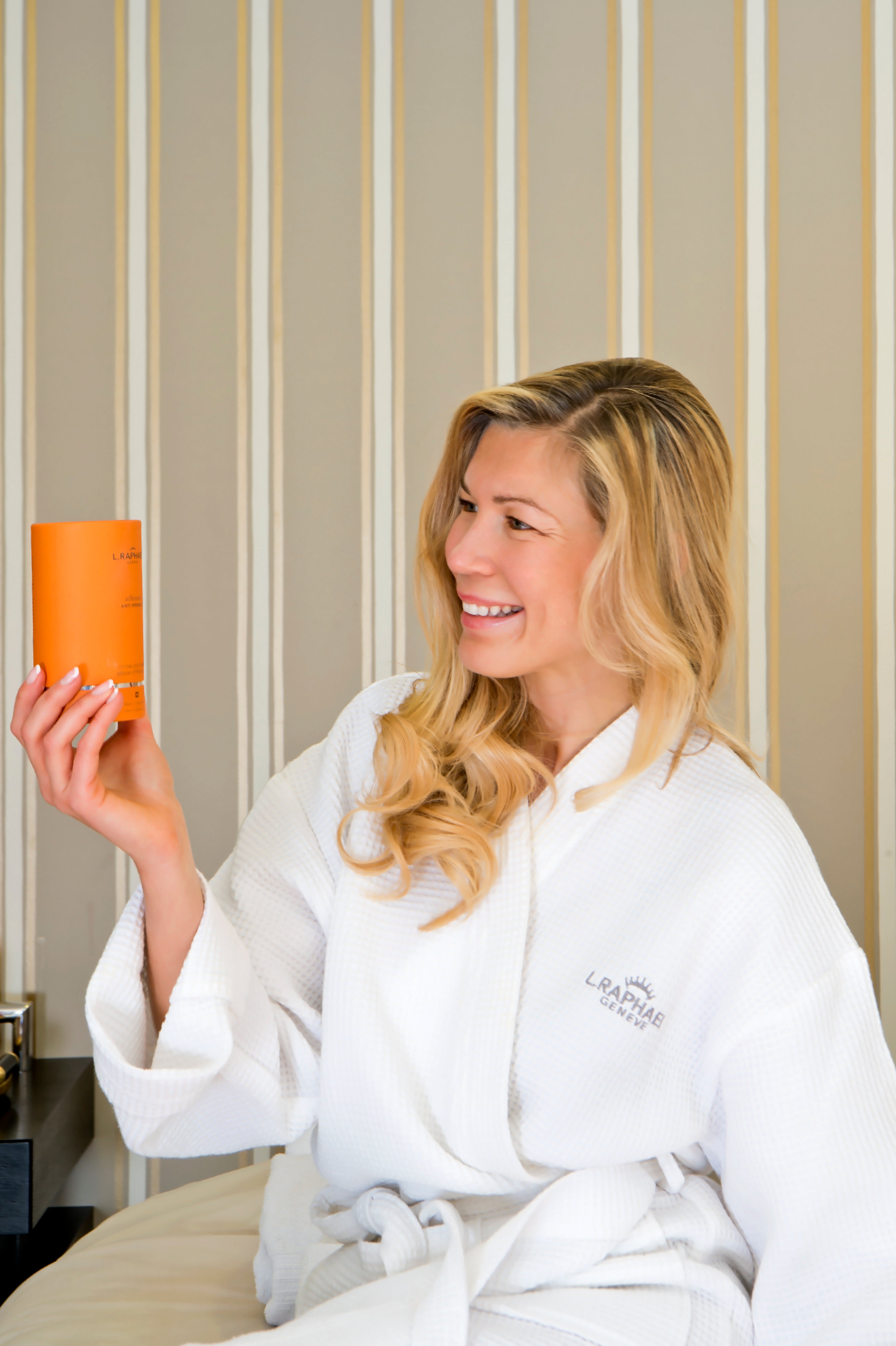 Woman in a white robe holding L.RAPHAEL Skin care product 