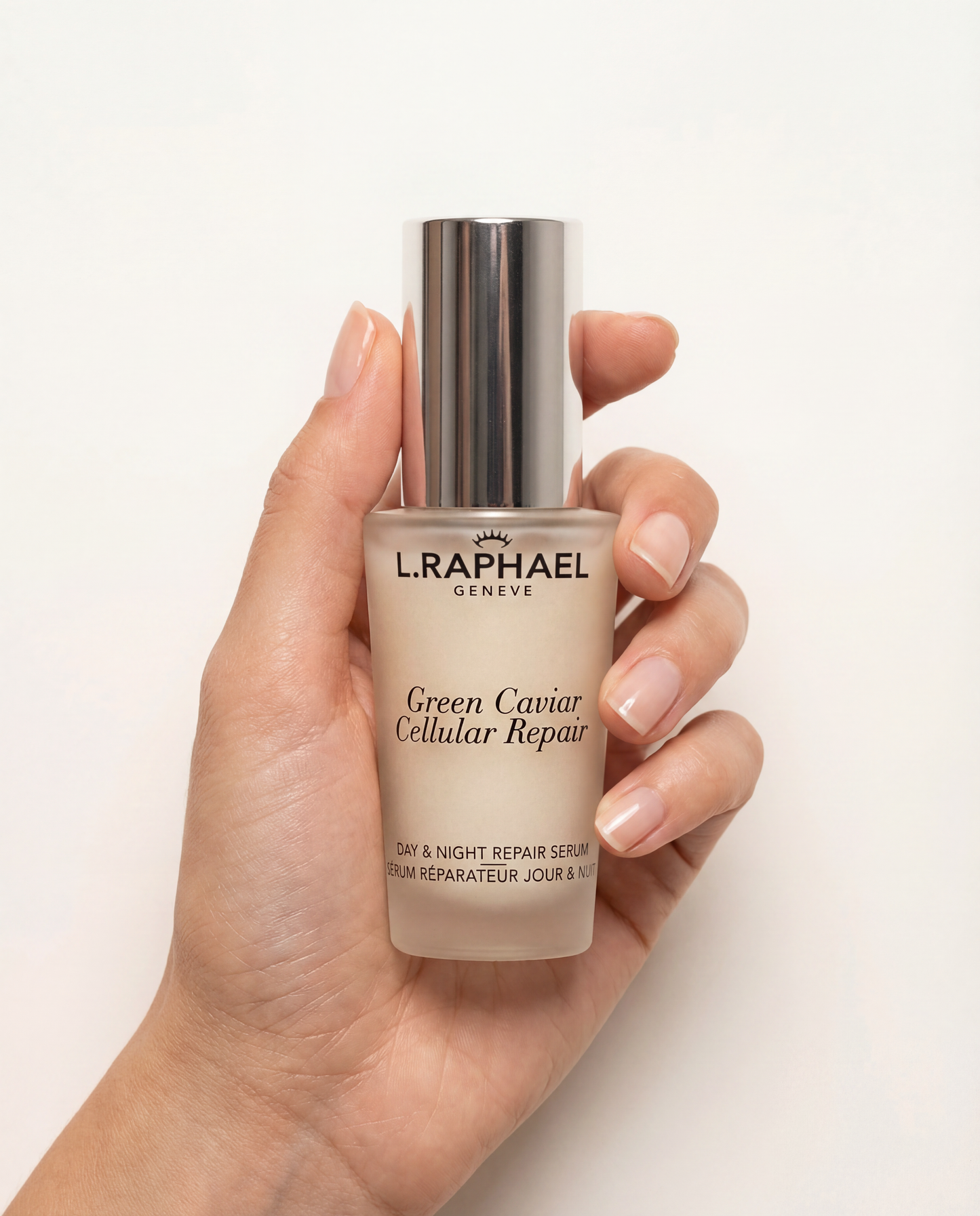 Hand holding a L.RAPHAEL skincare serum bottle on a white background